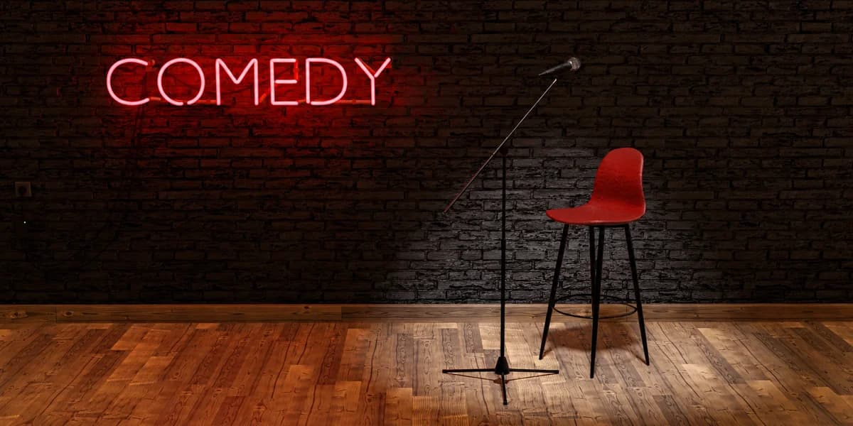 Generic stock atmosphere: a comedy stage with a red chair, microphone and neon Comedy sign, not this event or venue